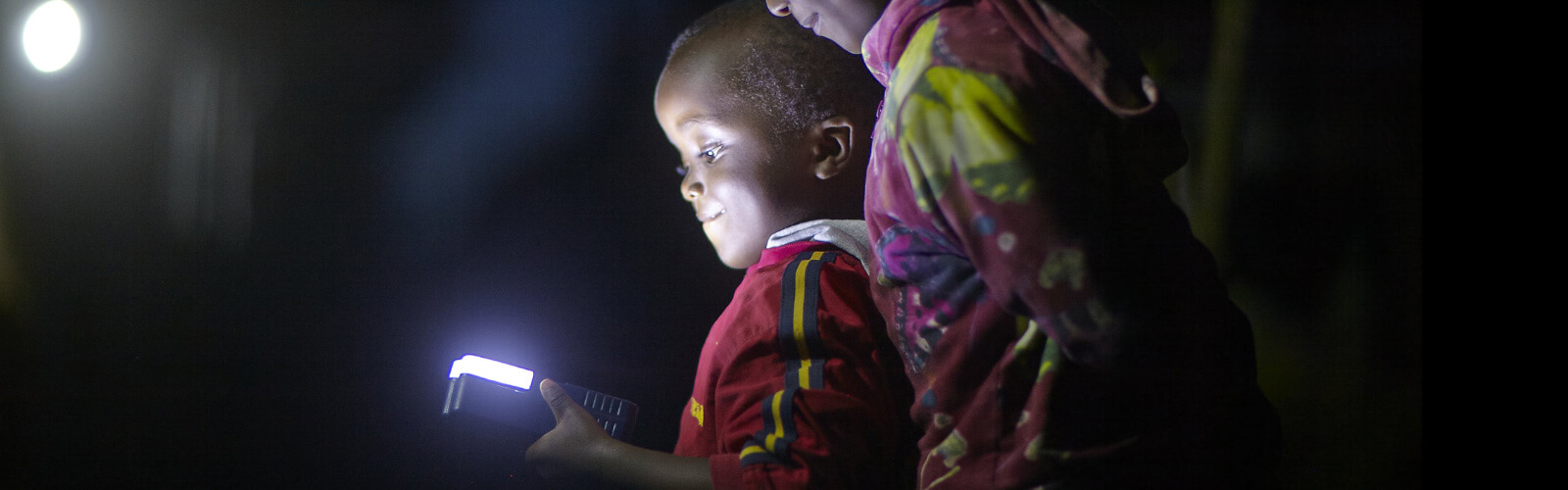 a child looking at a glowing handheld device in the dark